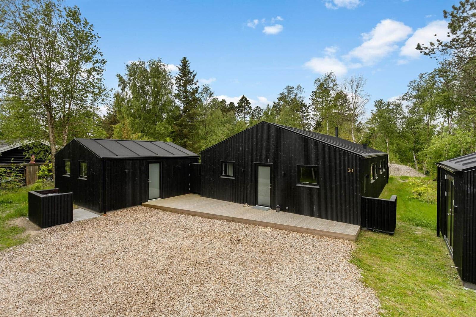 Schwarze Holzhütte mit Terrasse und Grasfläche im Wald