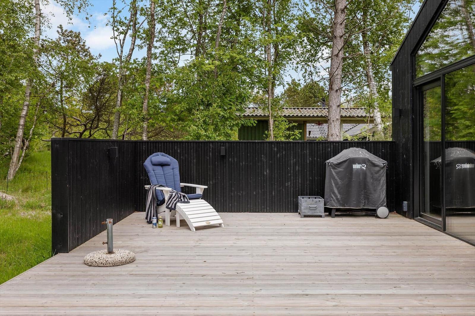 Terrasse mit Liegestuhl, Grill und Sicht auf Bäume.