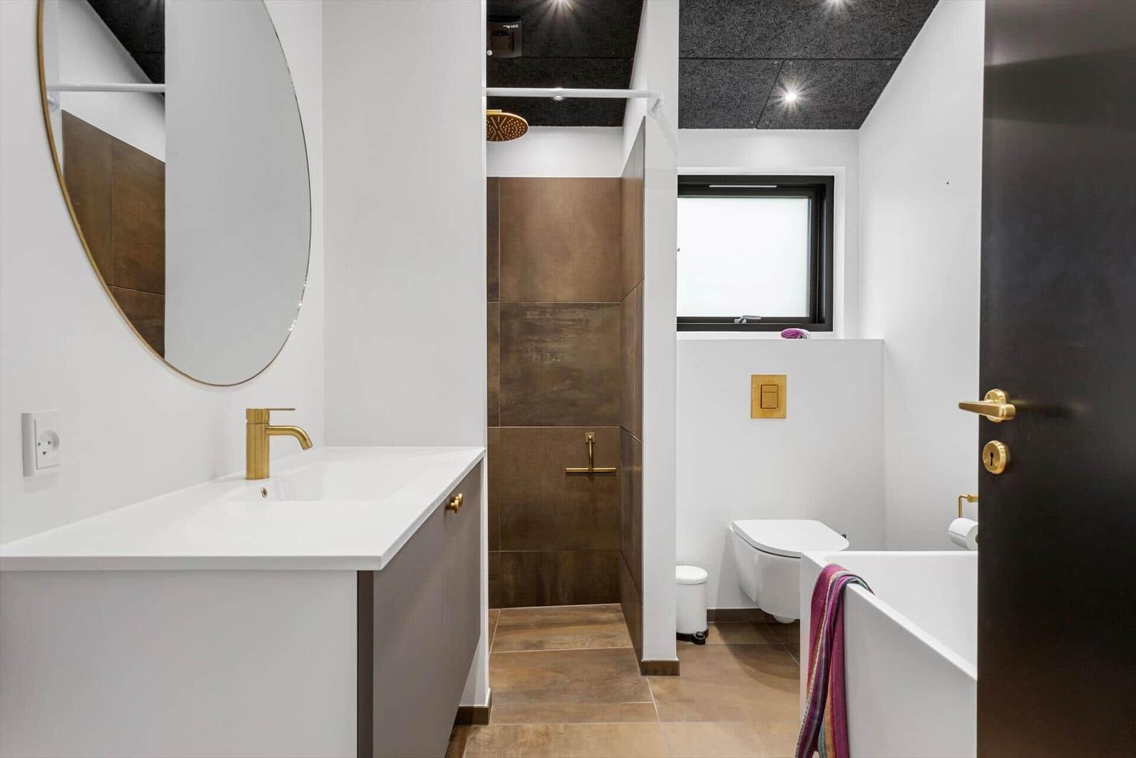 Badezimmer mit Waschbecken, Dusche und Toilette. Goldene Armaturen und runde Spiegel.