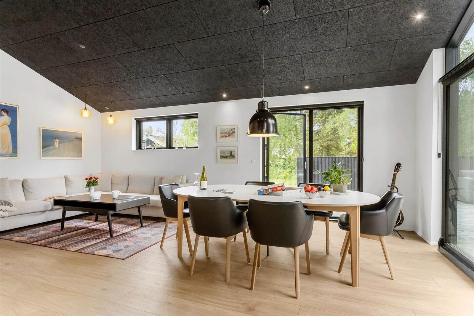 Wohn- und Essbereich mit Sofa, Tisch und Stühlen. Große Fenster und Glasfront.