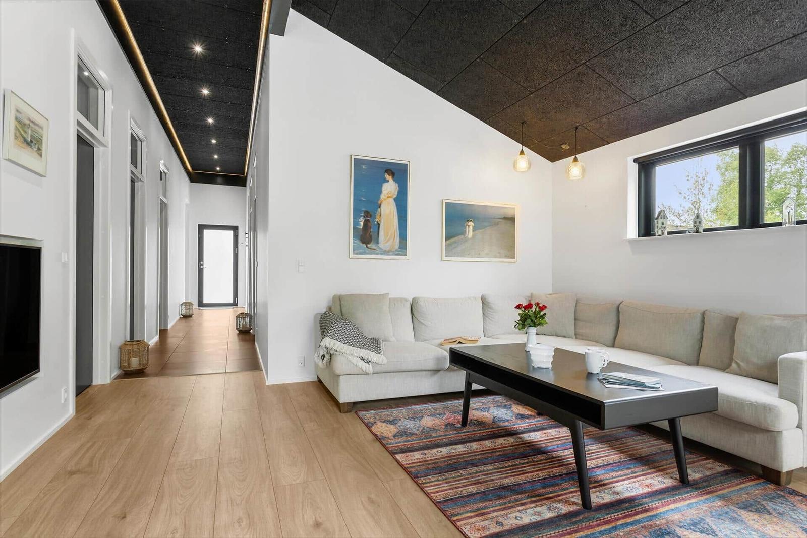 Wohnzimmer mit Sofa, Couchtisch und Wandbildern. Holzboden und schräger Deckenbereich.