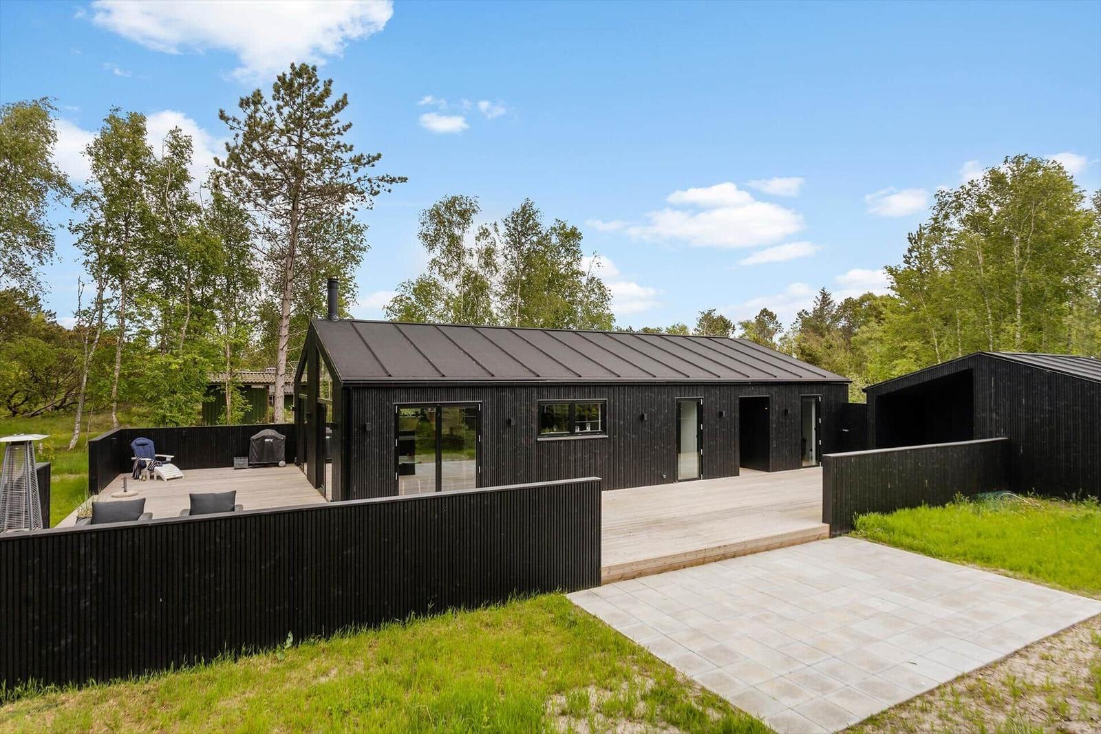 Moderne schwarze Hütte mit Terrasse und Grillplatz in grüner Umgebung.