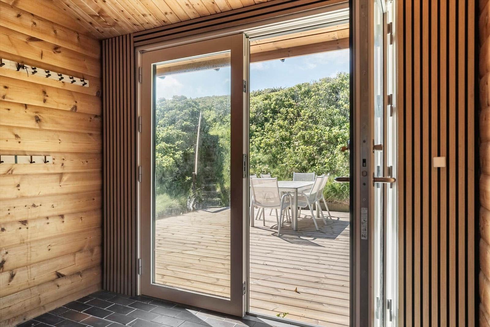 Holzverkleidete Tür führt auf eine Terrasse mit Tisch und Stühlen.