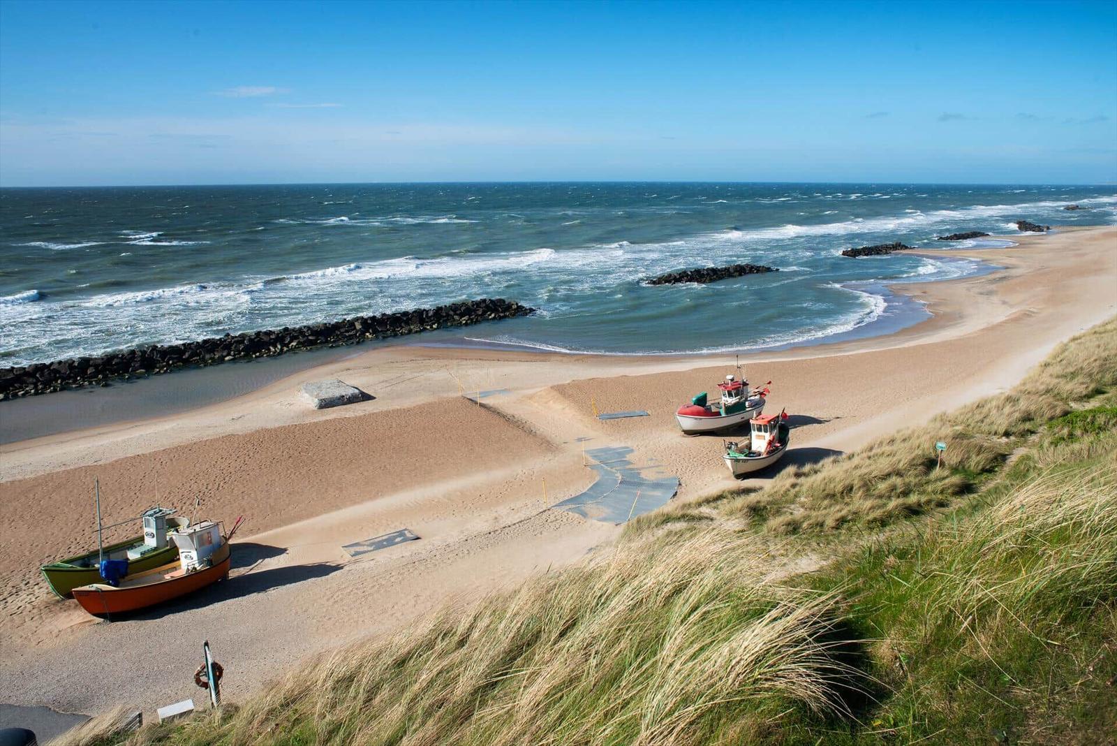 Strand mit Fischerbooten und Dünen unter blauem Himmel