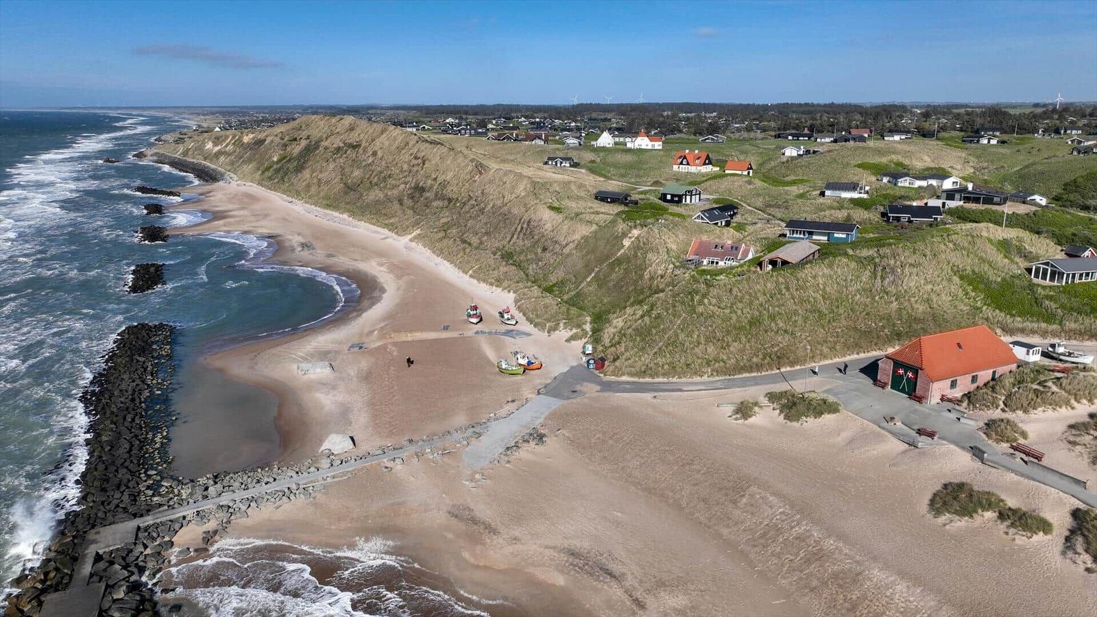 Strand mit Dünen, Häusern und Booten an der Küste.