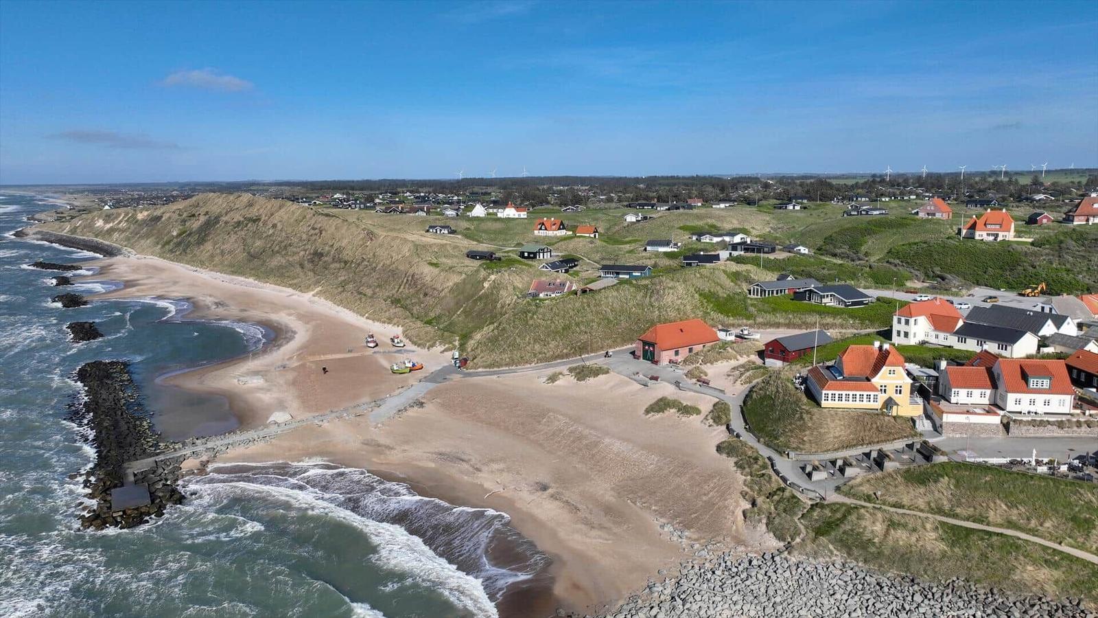 Strand mit Dünen und Häusern an der Küste unter blauem Himmel.