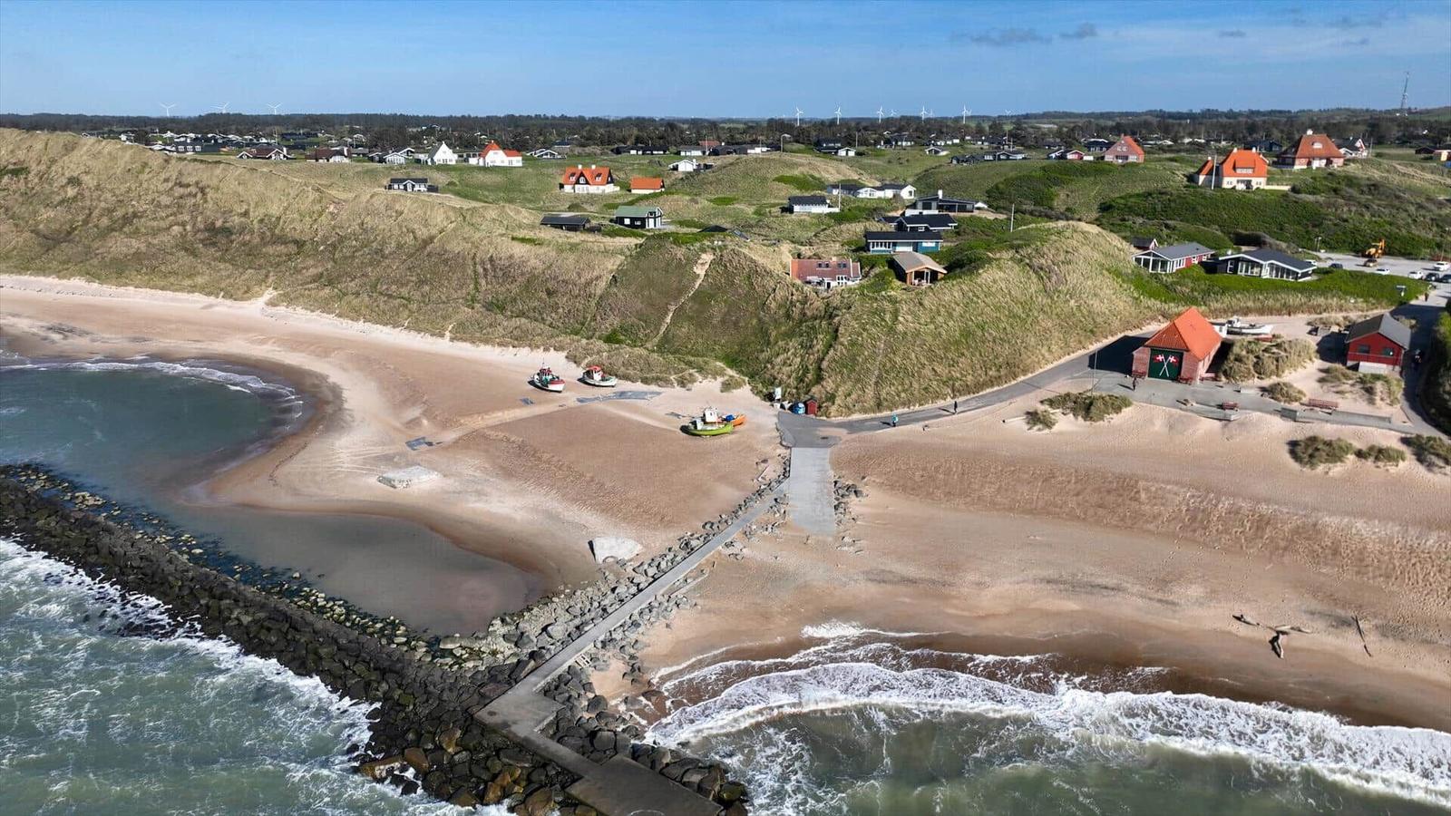 Strand mit Dünen, Booten und Häusern am Meer.