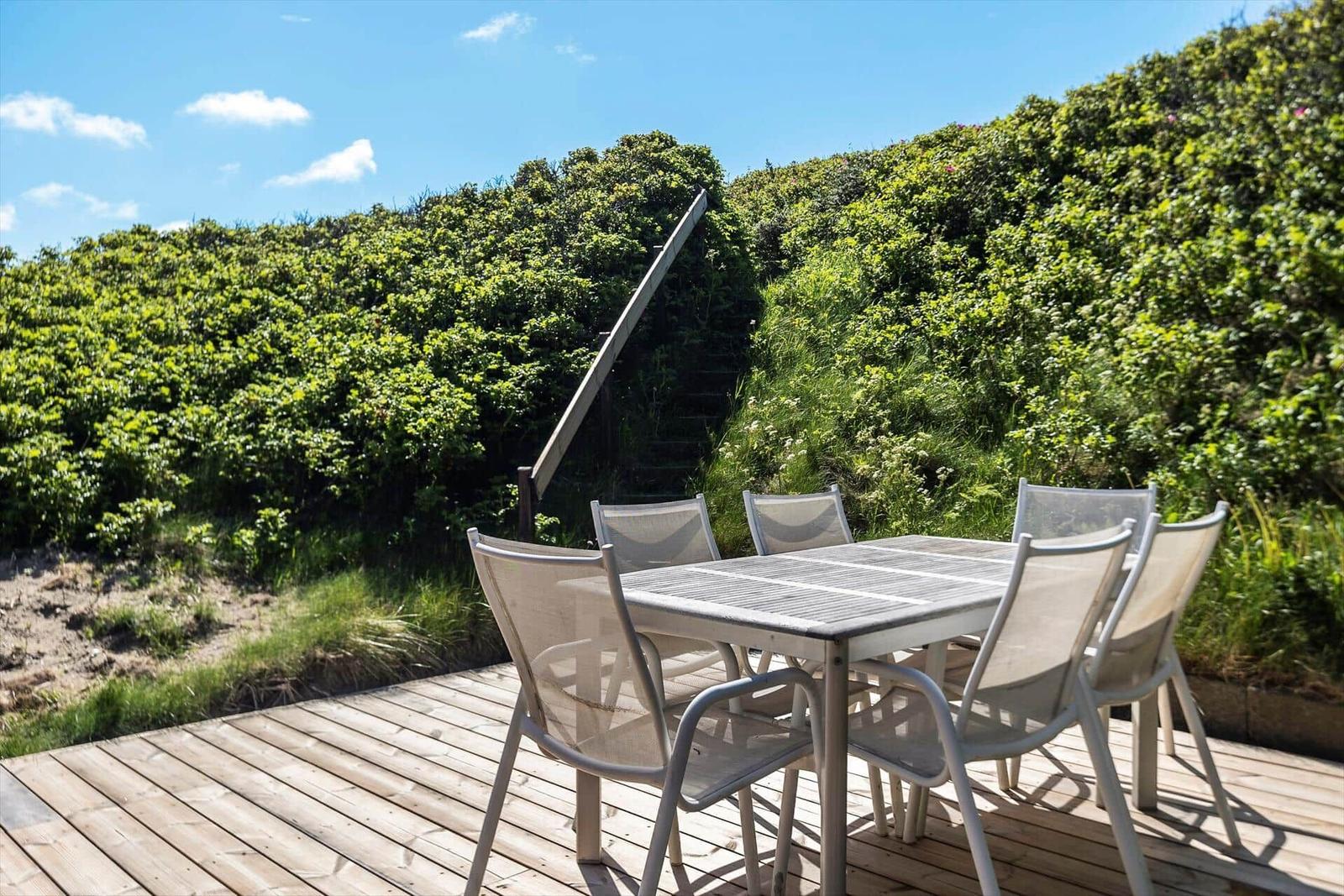 Holzterrasse mit Tisch und Stühlen, umgeben von grüner Vegetation und einem Holzgeländer.