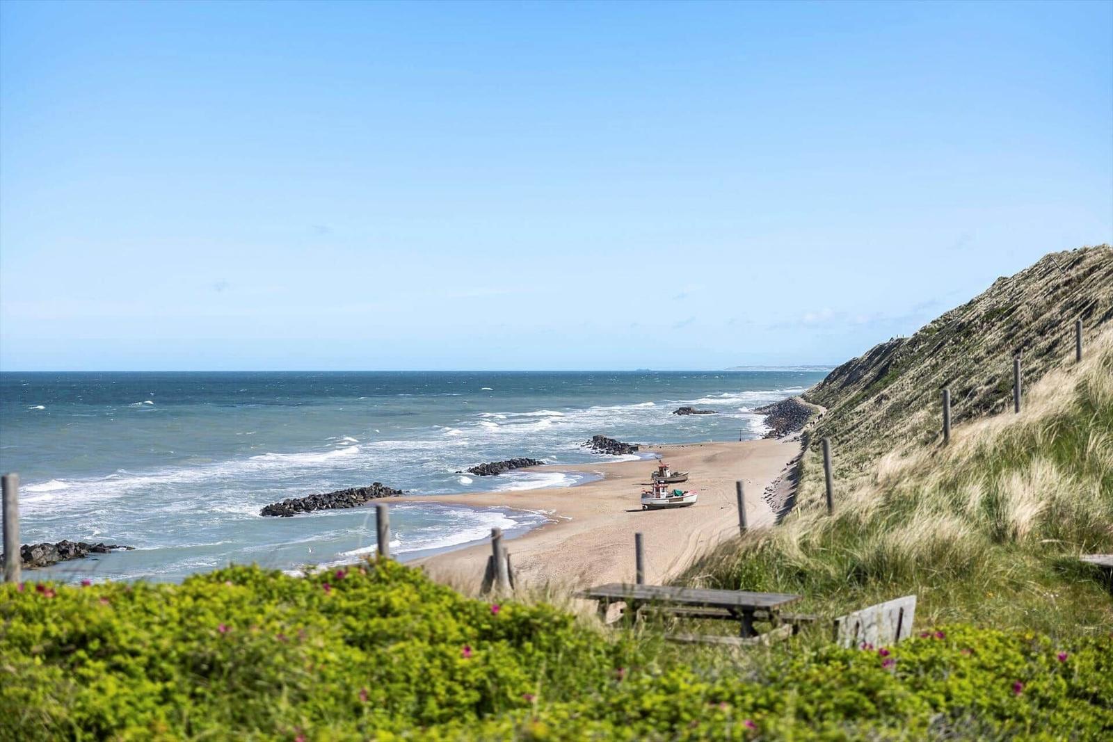 Strand mit Fischboot, Dünen und Meer unter blauem Himmel.