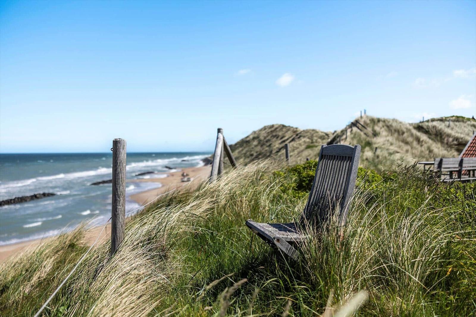 Holzstuhl auf Dünen mit Blick auf Strand und Meer.