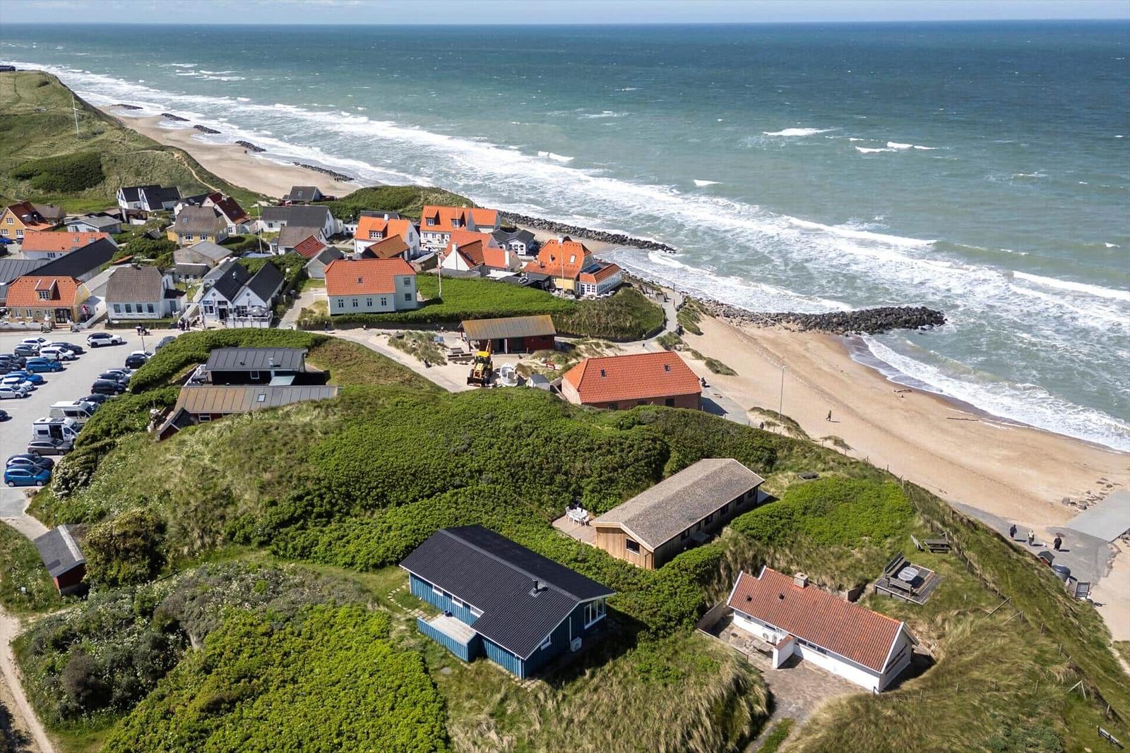 Dorf an der Küste mit Häusern und Strand. Grün bewachsene Dünen umgeben die Gebäude.