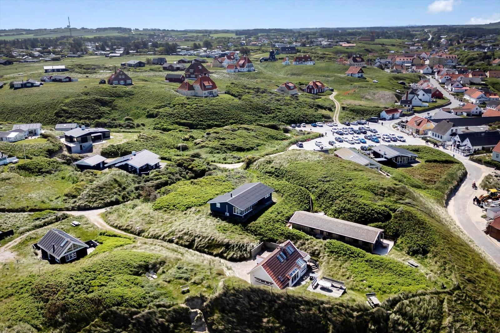 Luftbild von Ferienhäusern auf grünen Dünen mit Blick auf das Dorf.