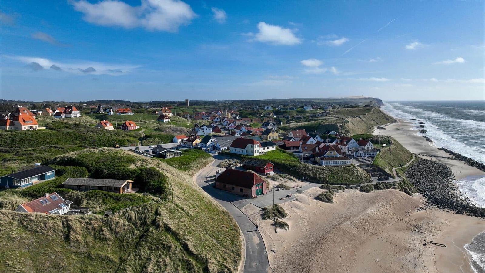 Dorf an der Küste mit Häusern auf grünen Hügeln und Sandstrand.