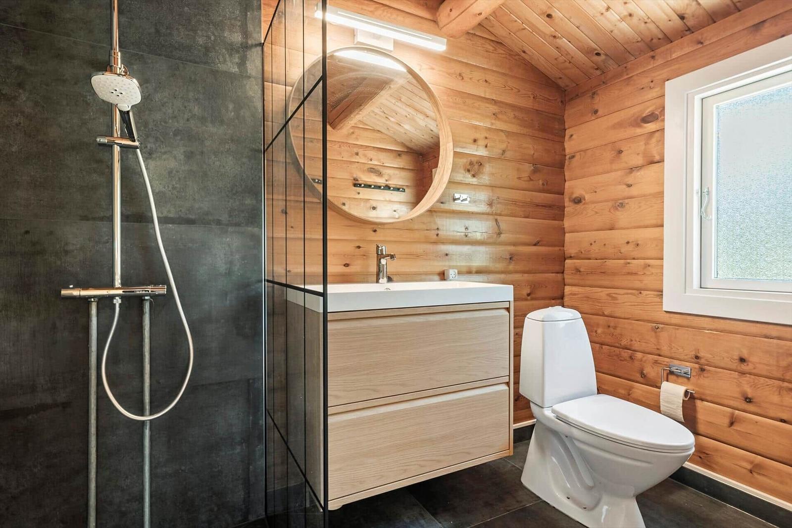 Bad mit Dusche, Waschbecken und Toilette. Holzwände und runder Spiegel.
