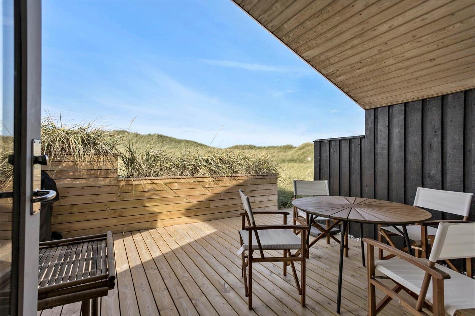 Terrace with table and chairs, view of dunes and sky.