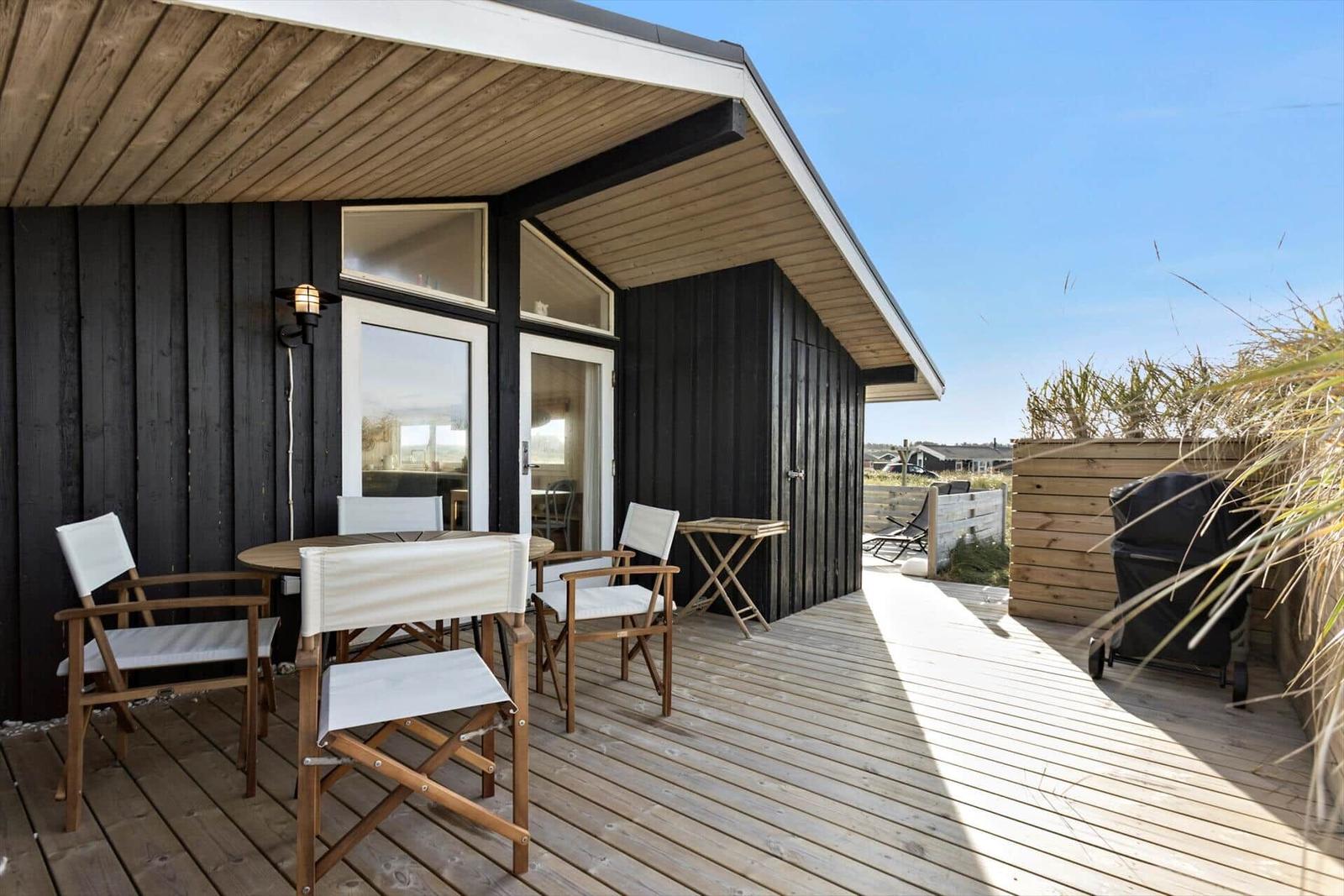 Deck with table and chairs in front of a wooden house with overhang.