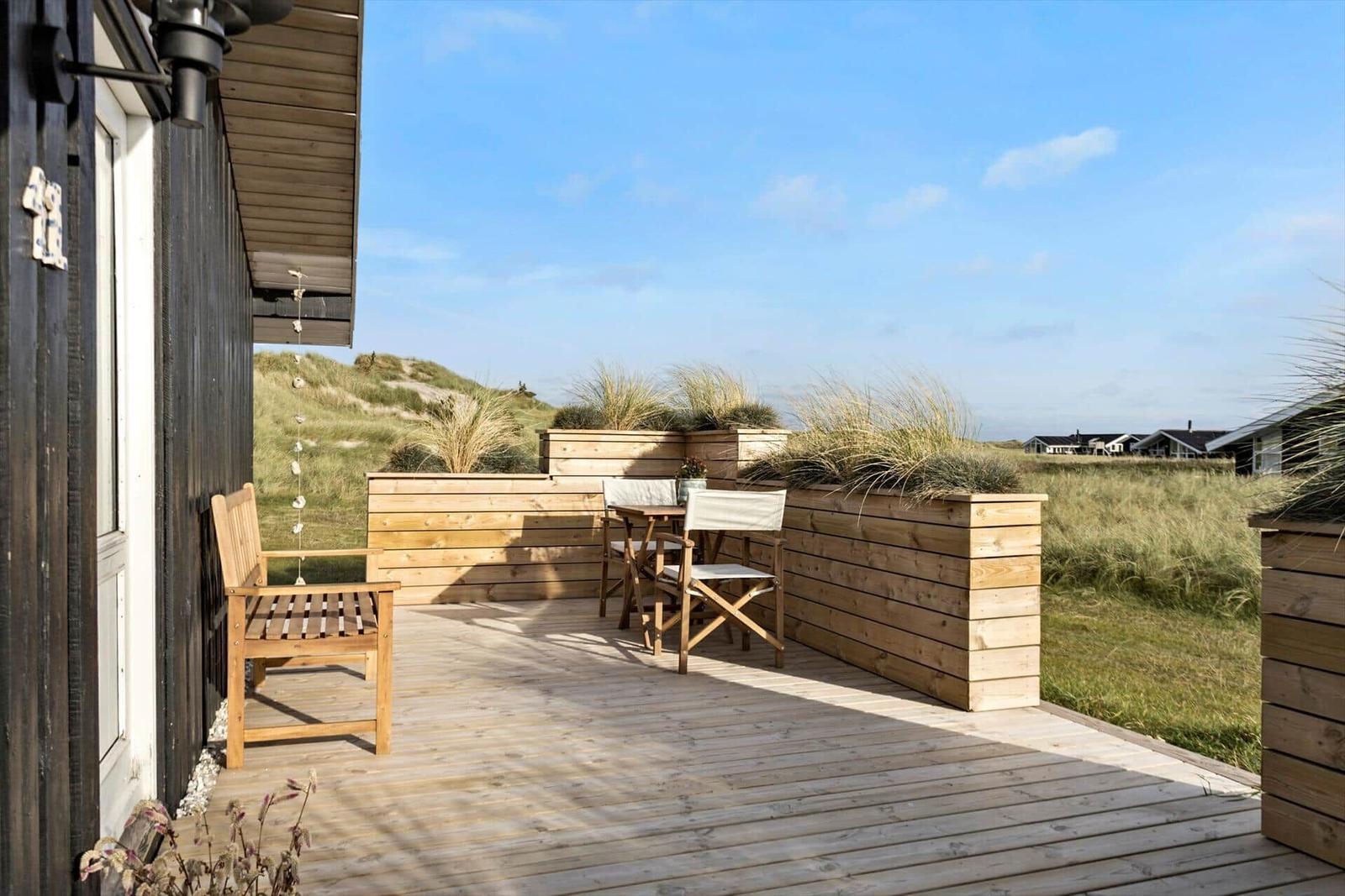 Wooden terrace with seating and view of dunes.