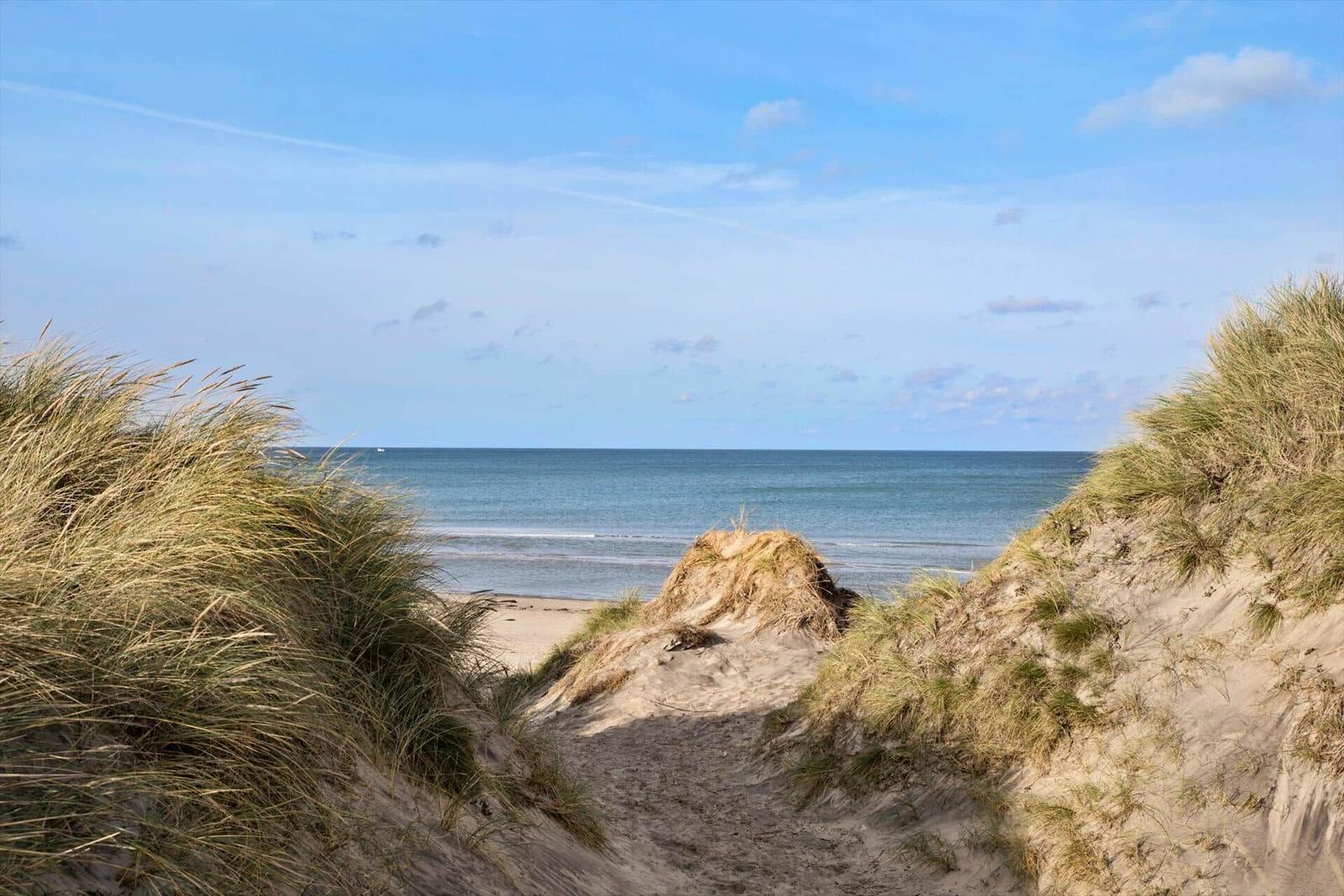 Sand dune path leads to the beach and sea under blue sky.