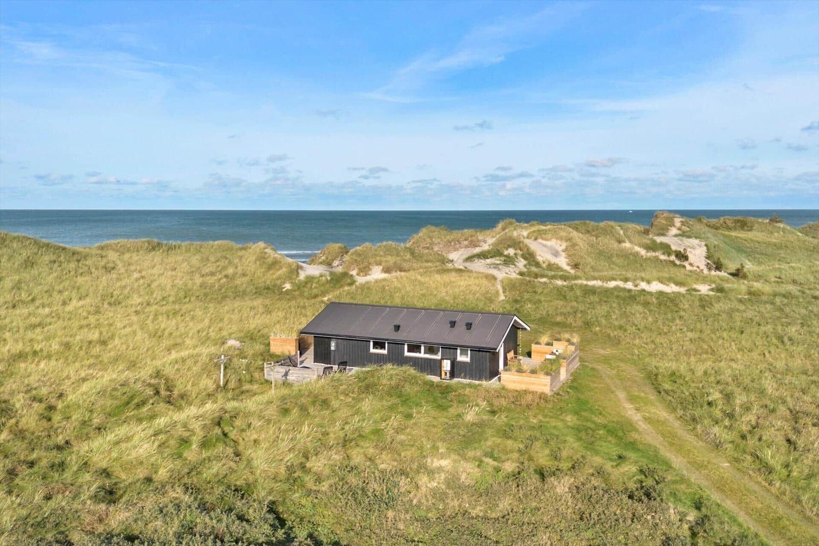 A black house on dunes with a view of the sea.