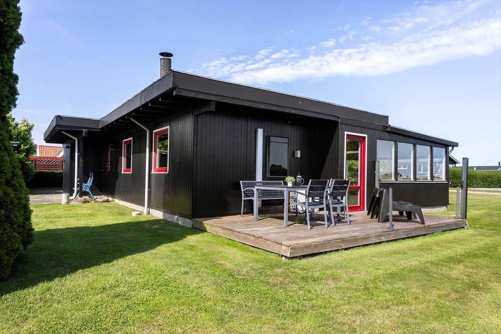 Black house with red door and deck with table and chairs.