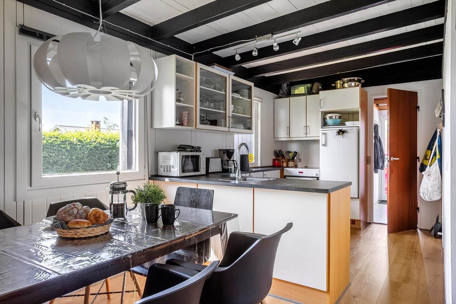 Kitchen with dining area, white cabinets, and black beams on ceiling.