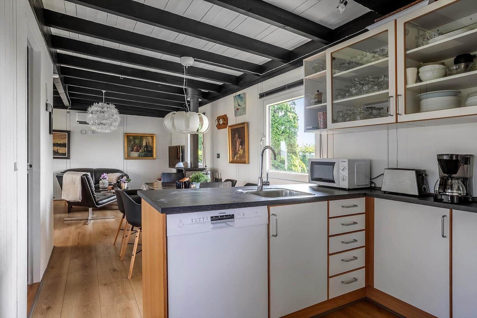 Kitchen with countertop, sink, and dishes. In the background, living area with sofa and window.