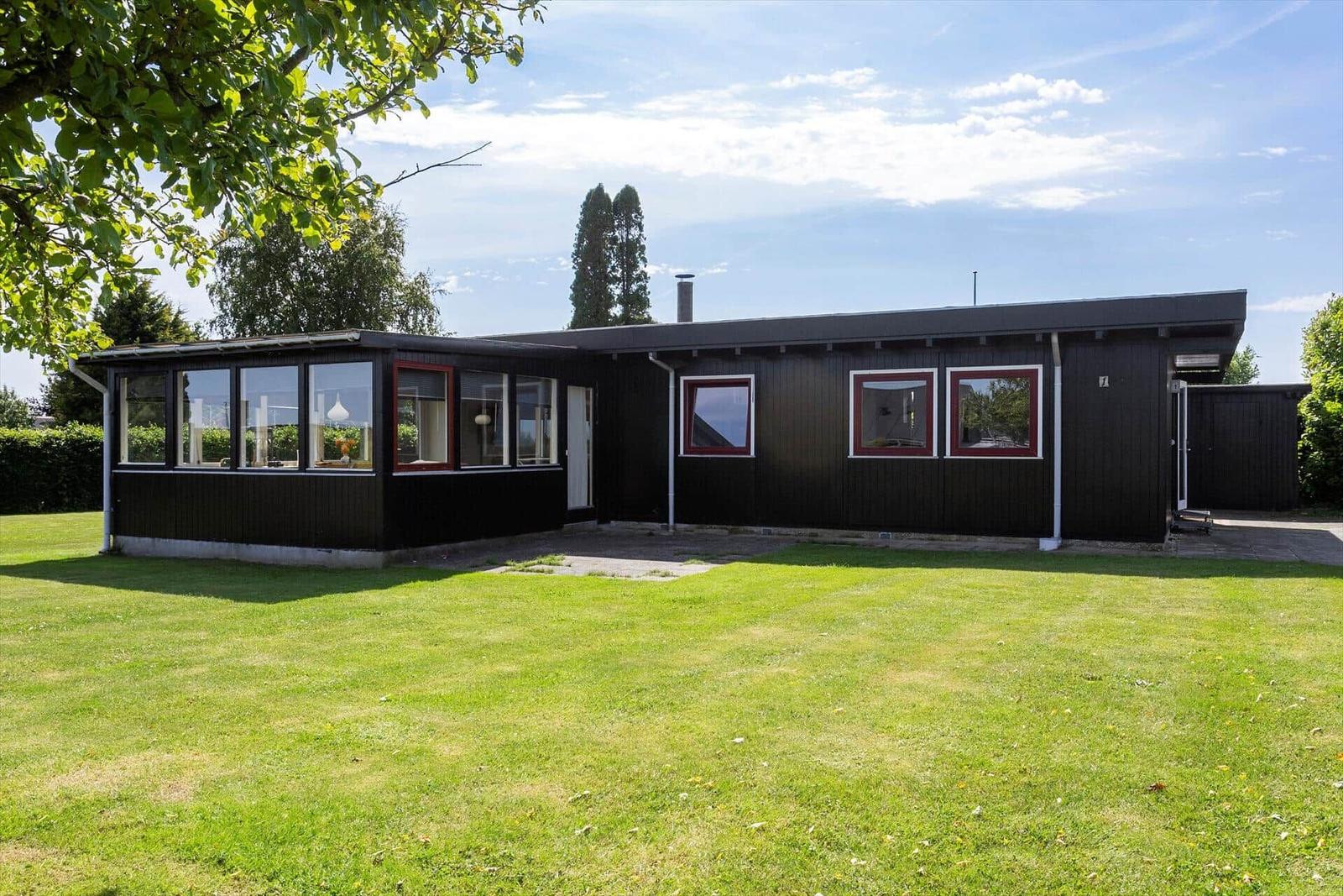 A black house with red window frames and a green lawn.