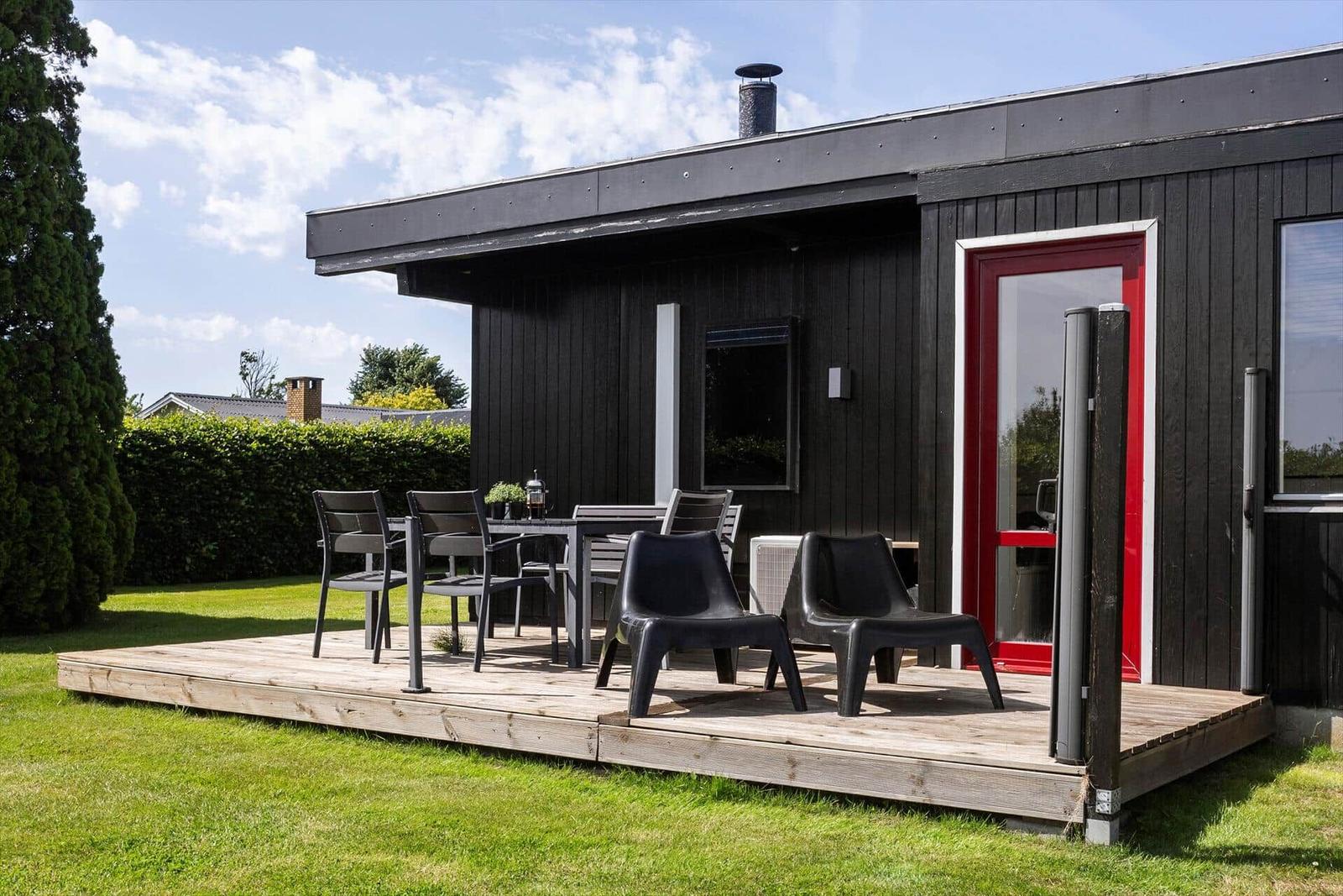 Black wooden house with red door and terrace with seating.