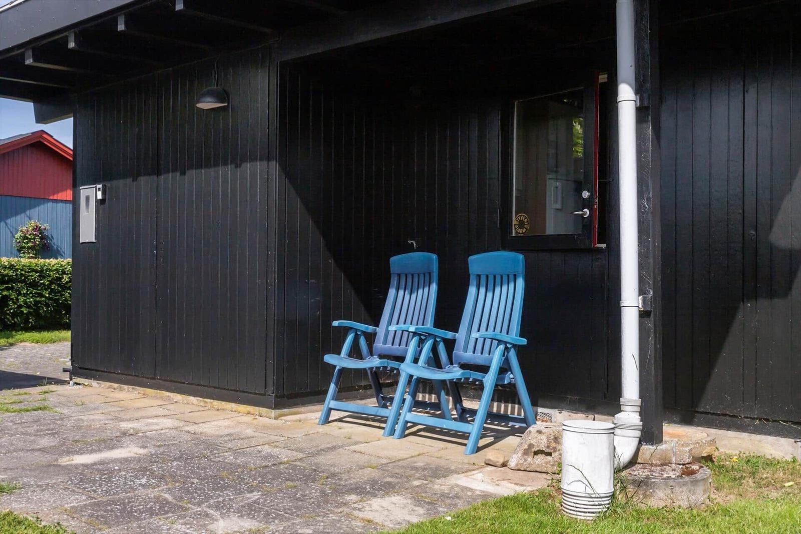 Two blue chairs stand before a black house with door and window.
