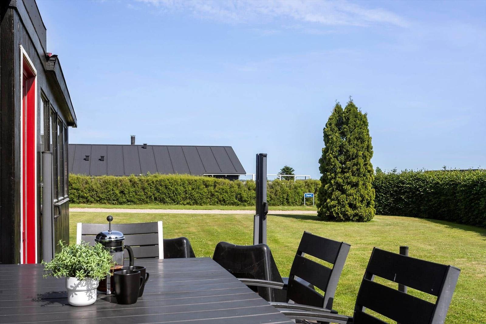 Terrace with table and chairs, view of green lawn and a tree.