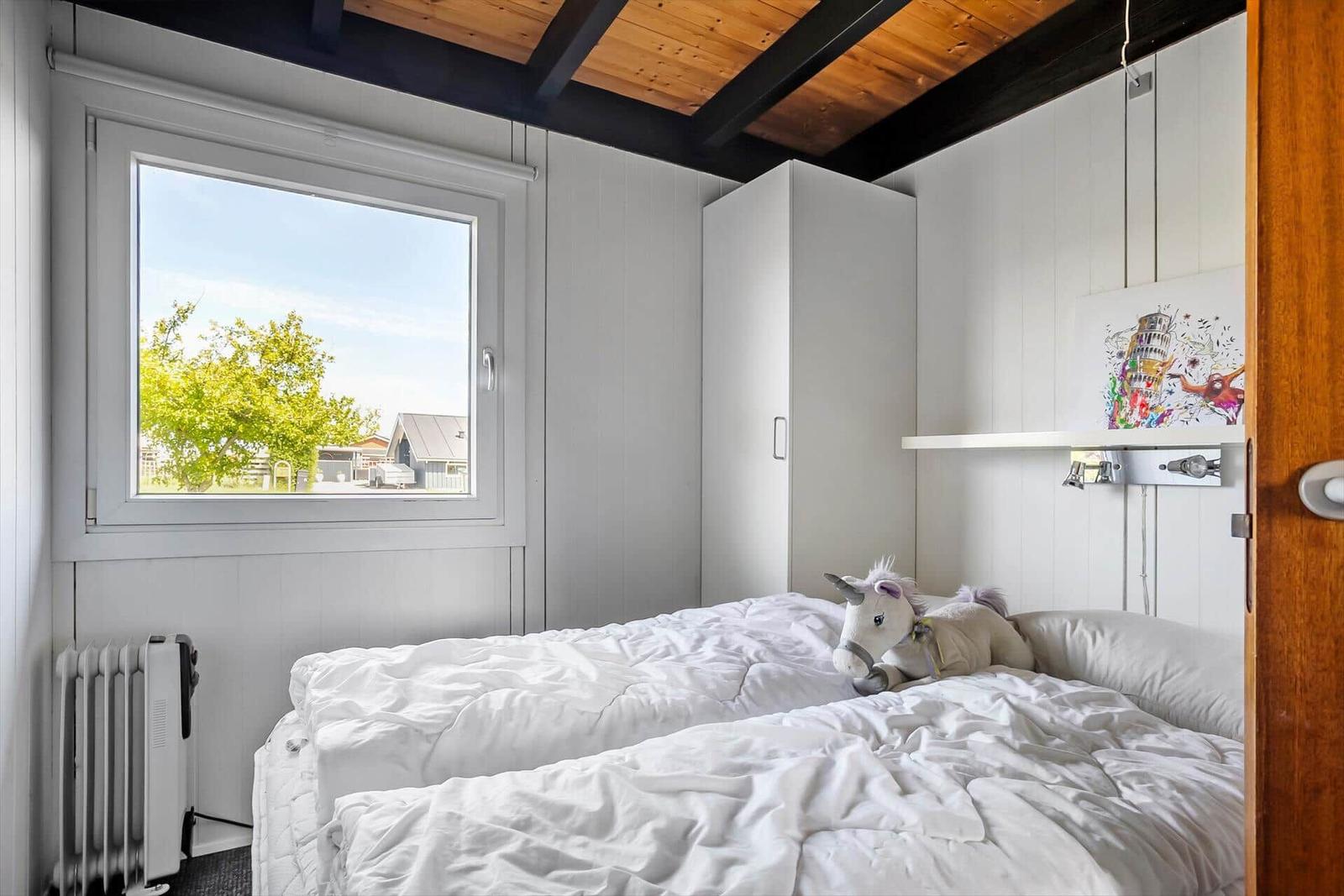 Bedroom with white bed, window, and wooden ceiling.