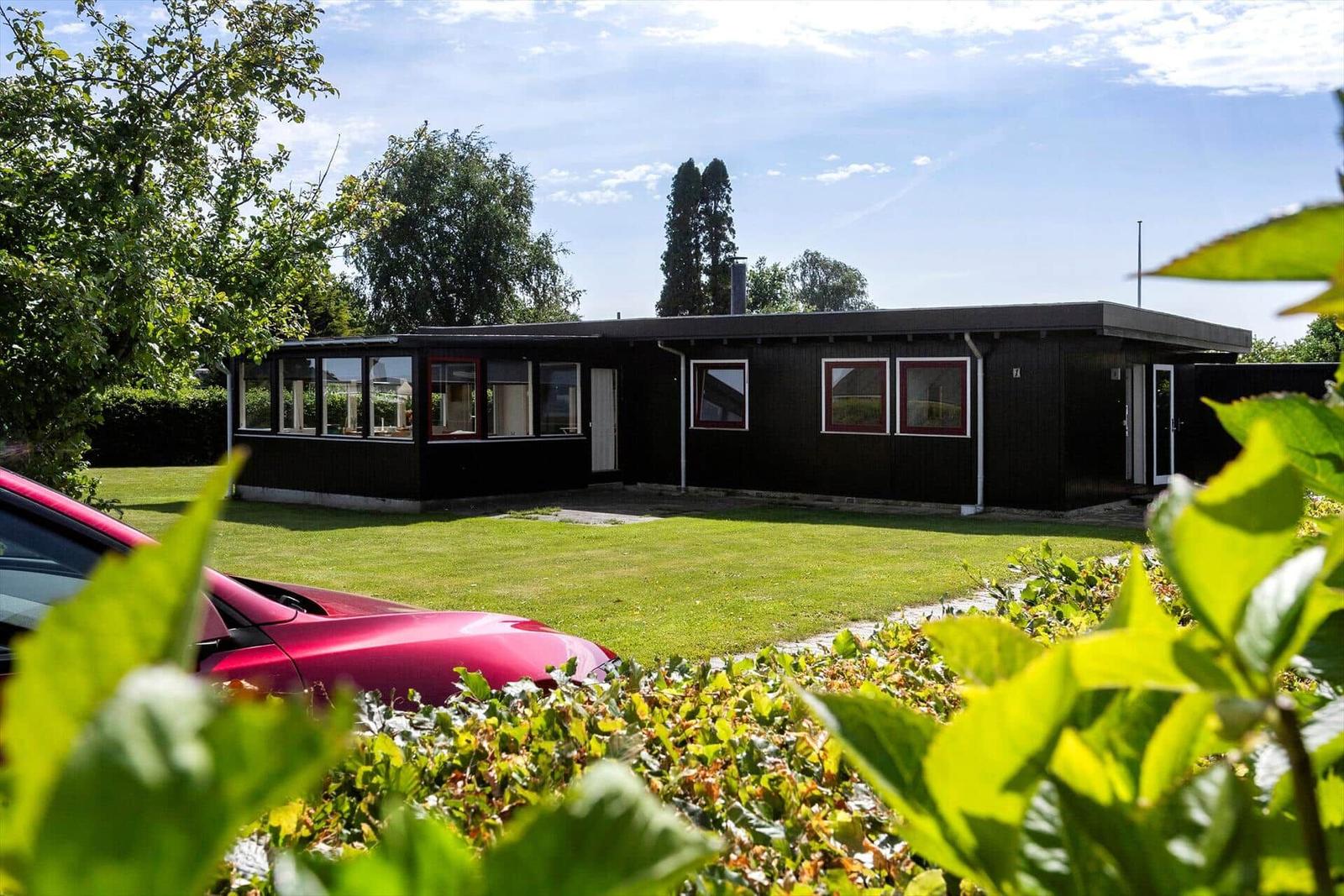 Modern black villa with large garden and red car in front.