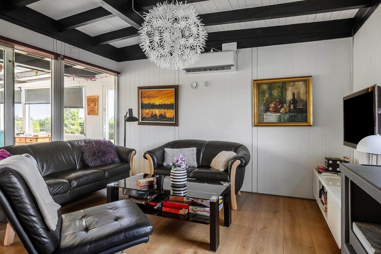 Living room with leather sofa, glass table, and wooden floor. Ceiling with dark beams and white walls.