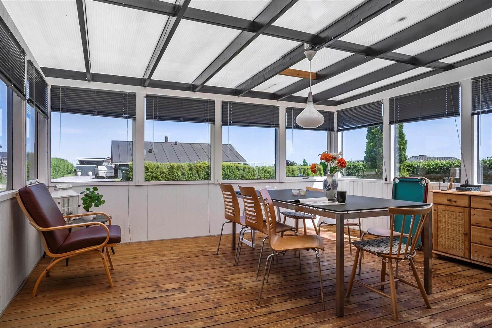 Glass roof with seating and dining table. Wooden floor and window front.