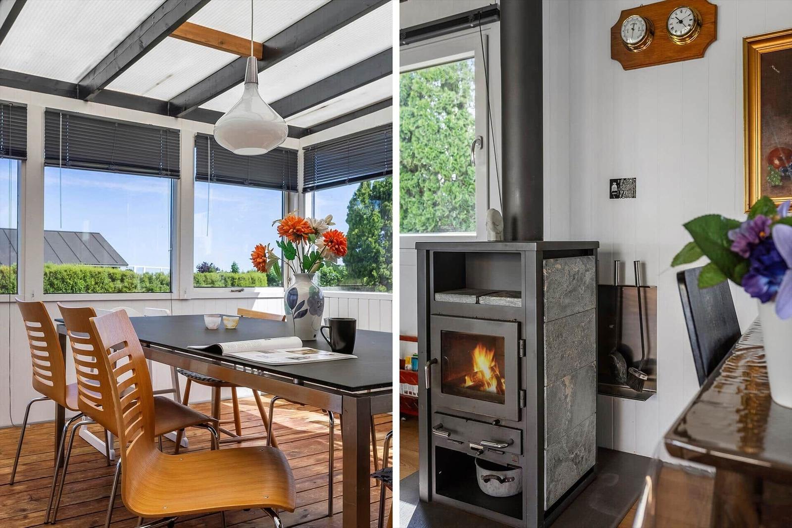 Dining area with table, chairs, and view of greenery. Wood stove with burning fire.