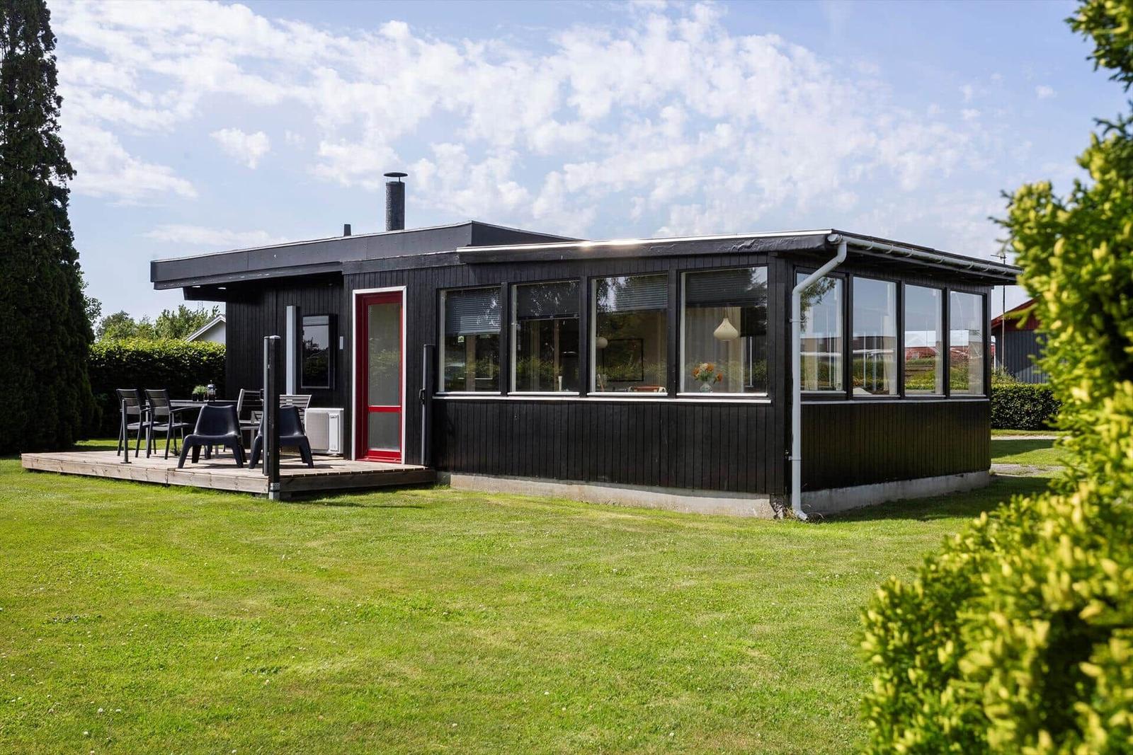 Black house with red door and terrace with table and chairs.