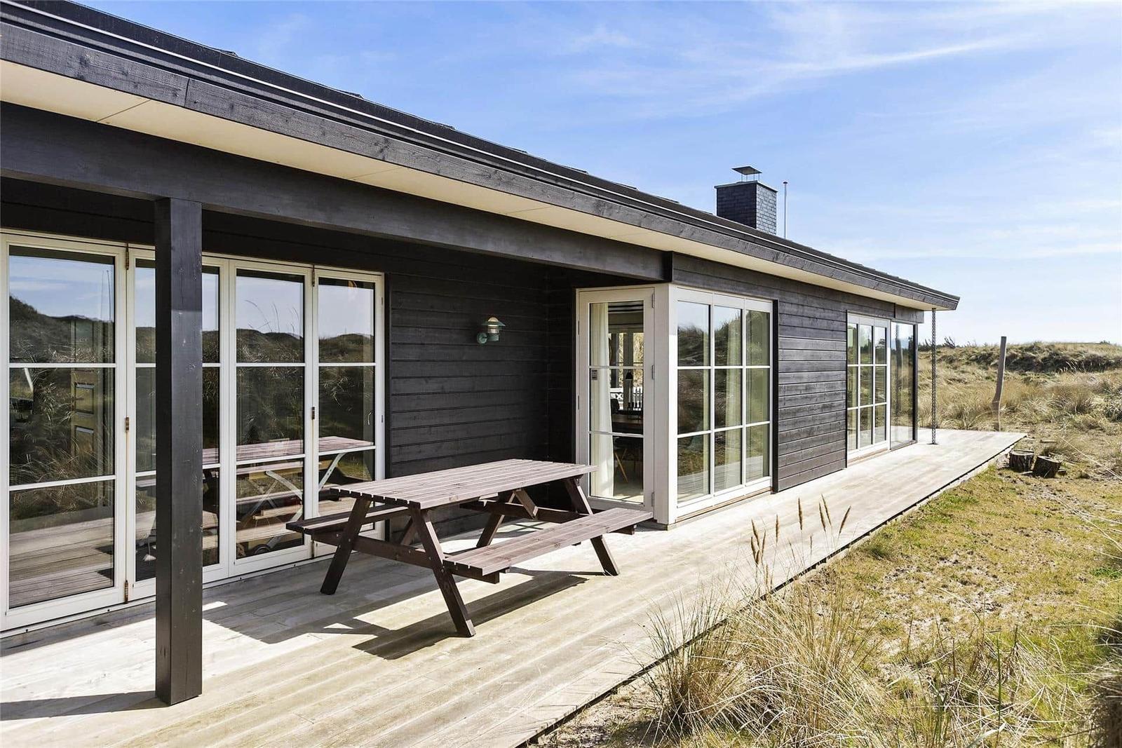 Modern wooden cabin with terrace and picnic table near the beach.