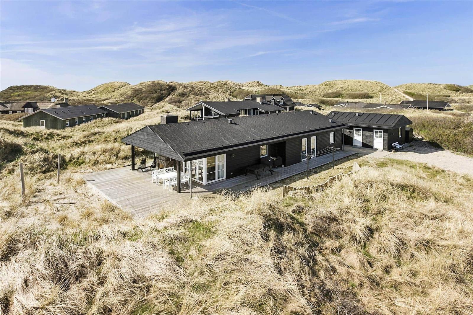Modern beach house with terrace and grill area between dunes.
