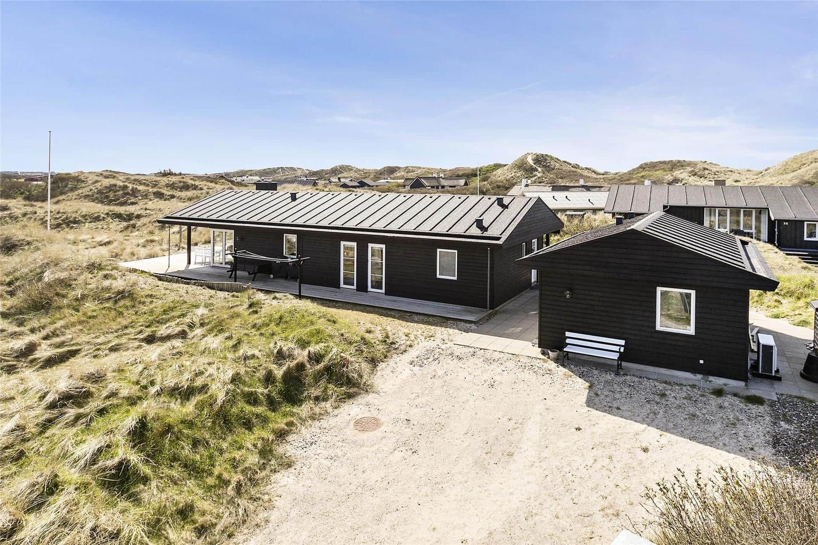Two black wooden houses with terrace and roof terrace in dune landscape.
