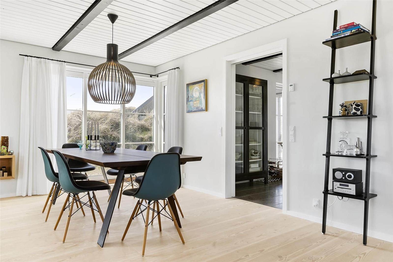 Dining area with table, chairs, and pendant lamp. Passage to kitchen. Shelf with decorative items.