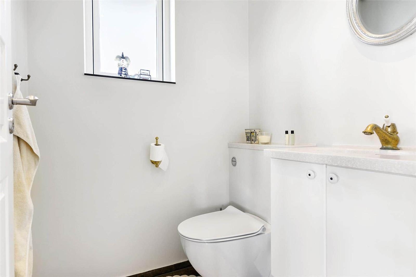 Bathroom with toilet, sink, and mirror. Window and towel rack visible.