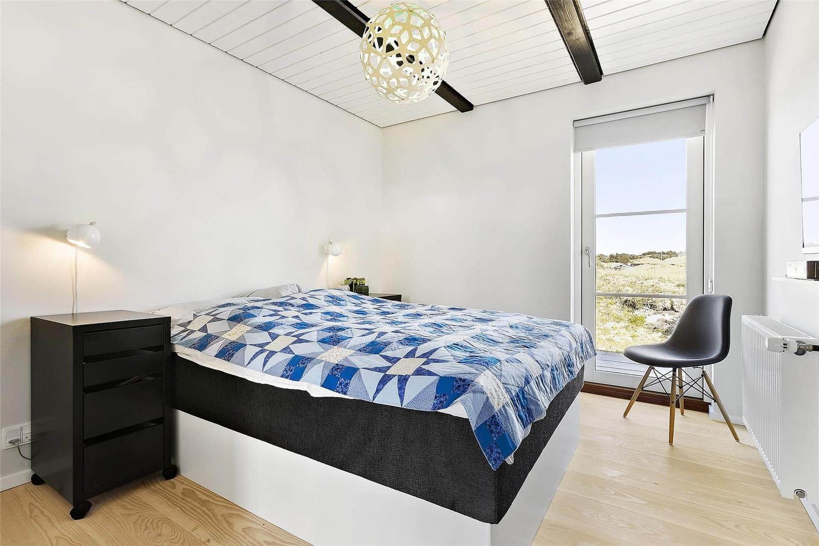 Bedroom with bed, nightstand, and chair. Window with view of landscape.