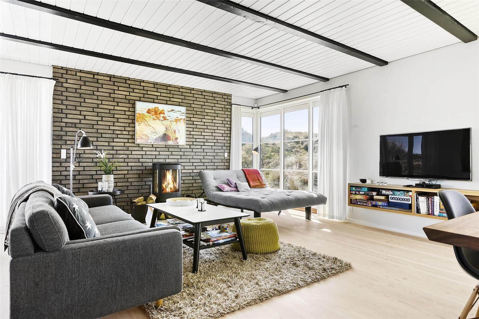 Living room with fireplace, sofa, and TV. Large windows with view of the landscape.