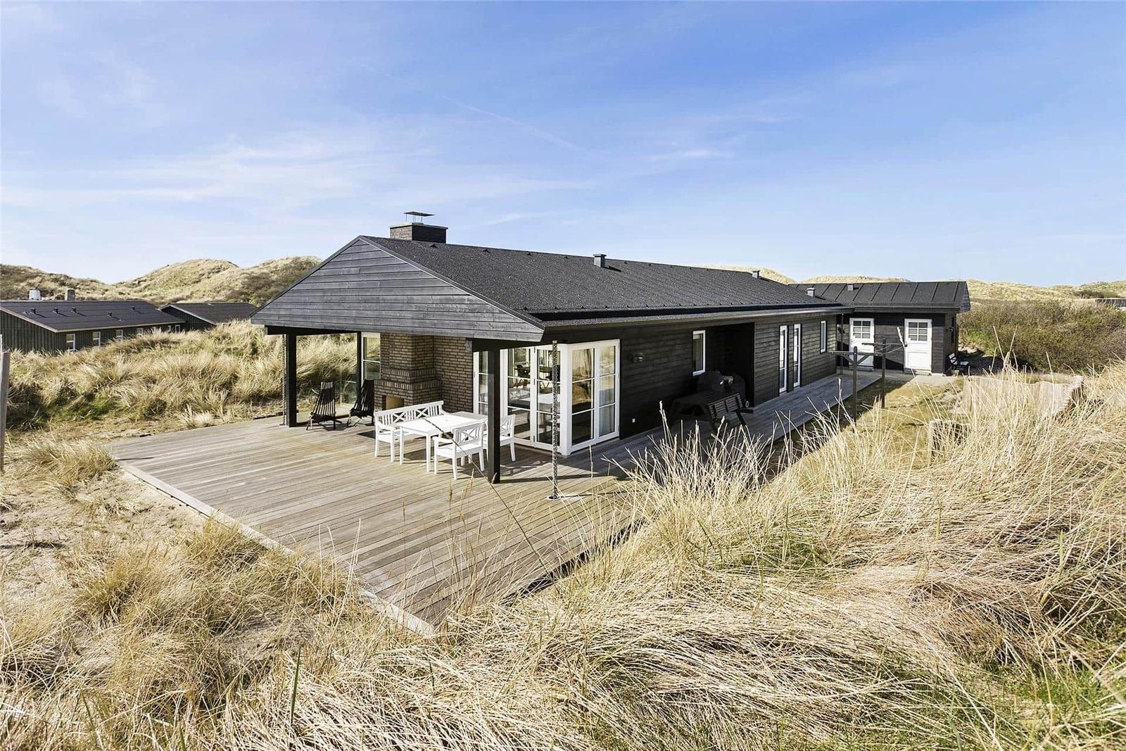 Modern villa with wooden terrace and garden furniture in dune landscape.
