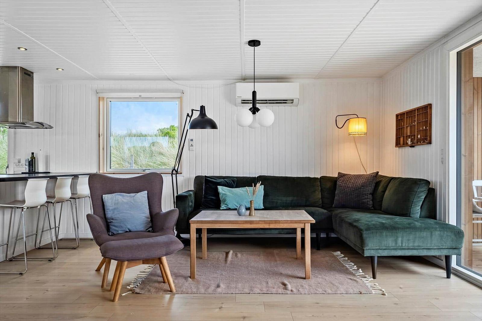 Wohnzimmer mit grünem Sofa, Holztisch und Stühlen. Küche mit Bar und Fenster.