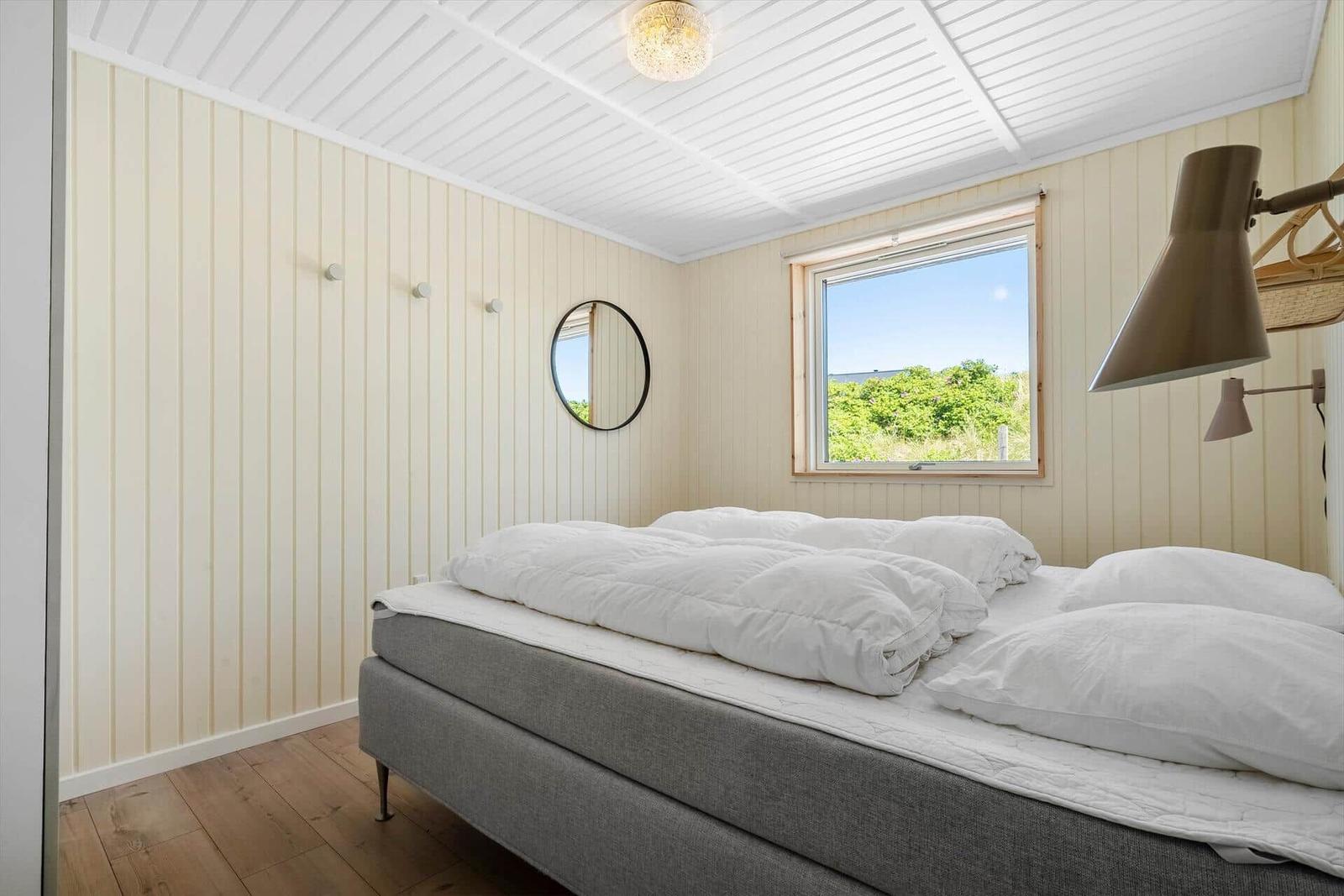 Schlafzimmer mit Bett, Fenster und Wandspiegel.