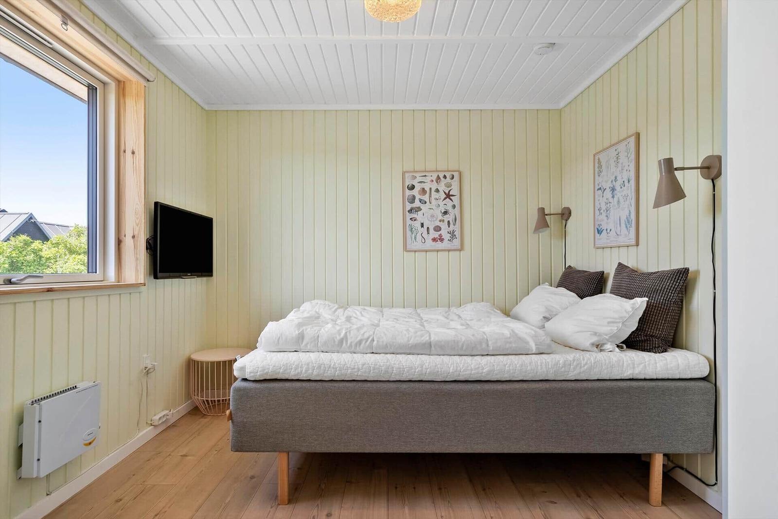 Schlafzimmer mit Bett, Wandbildern und Fenster. Holzboden und weiße Decke.