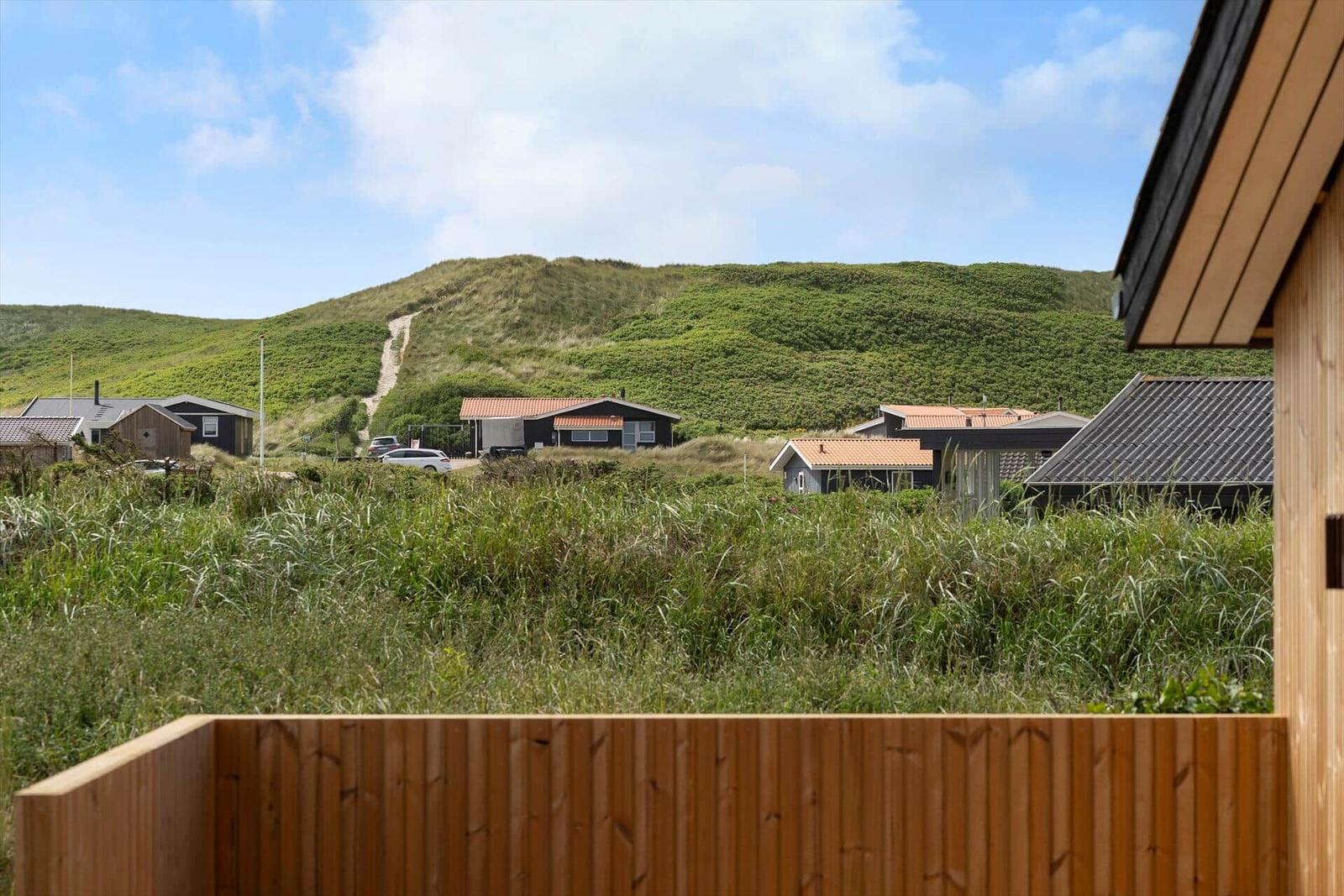 Von der Terrasse blickt man auf grüne Dünen und Ferienhäuser.