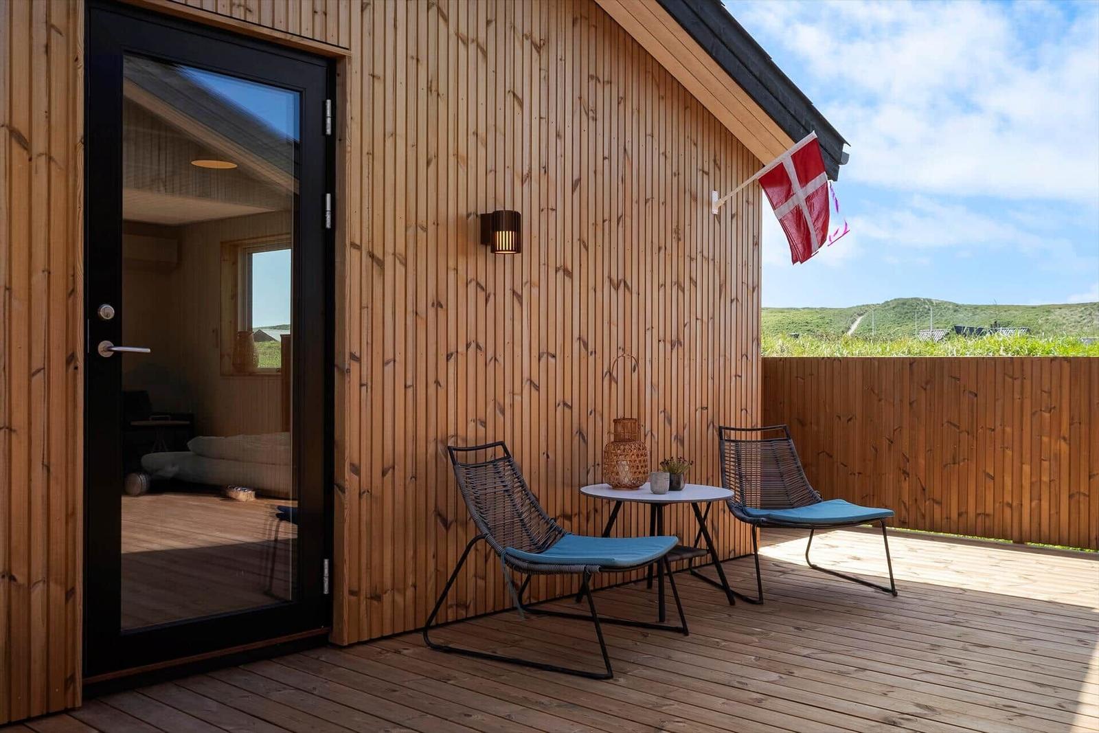 Terrasse mit zwei Stühlen und Tisch, daneben Flagge und Holzwand