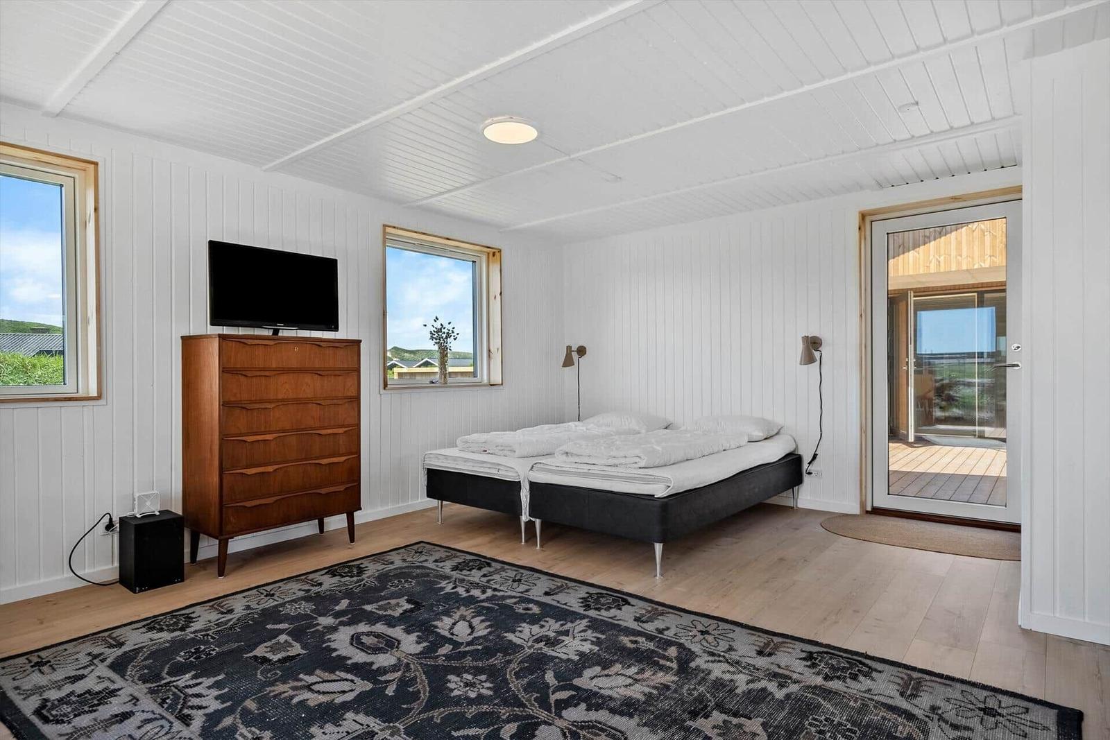 Schlafzimmer mit Doppelbett, Fernseher und Terrassenzugang.